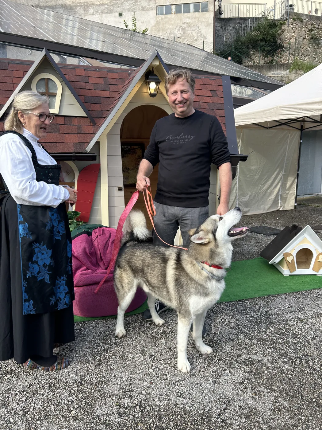 Signora in abito tradizionale e husky malamute davanti a casette in esposizione.