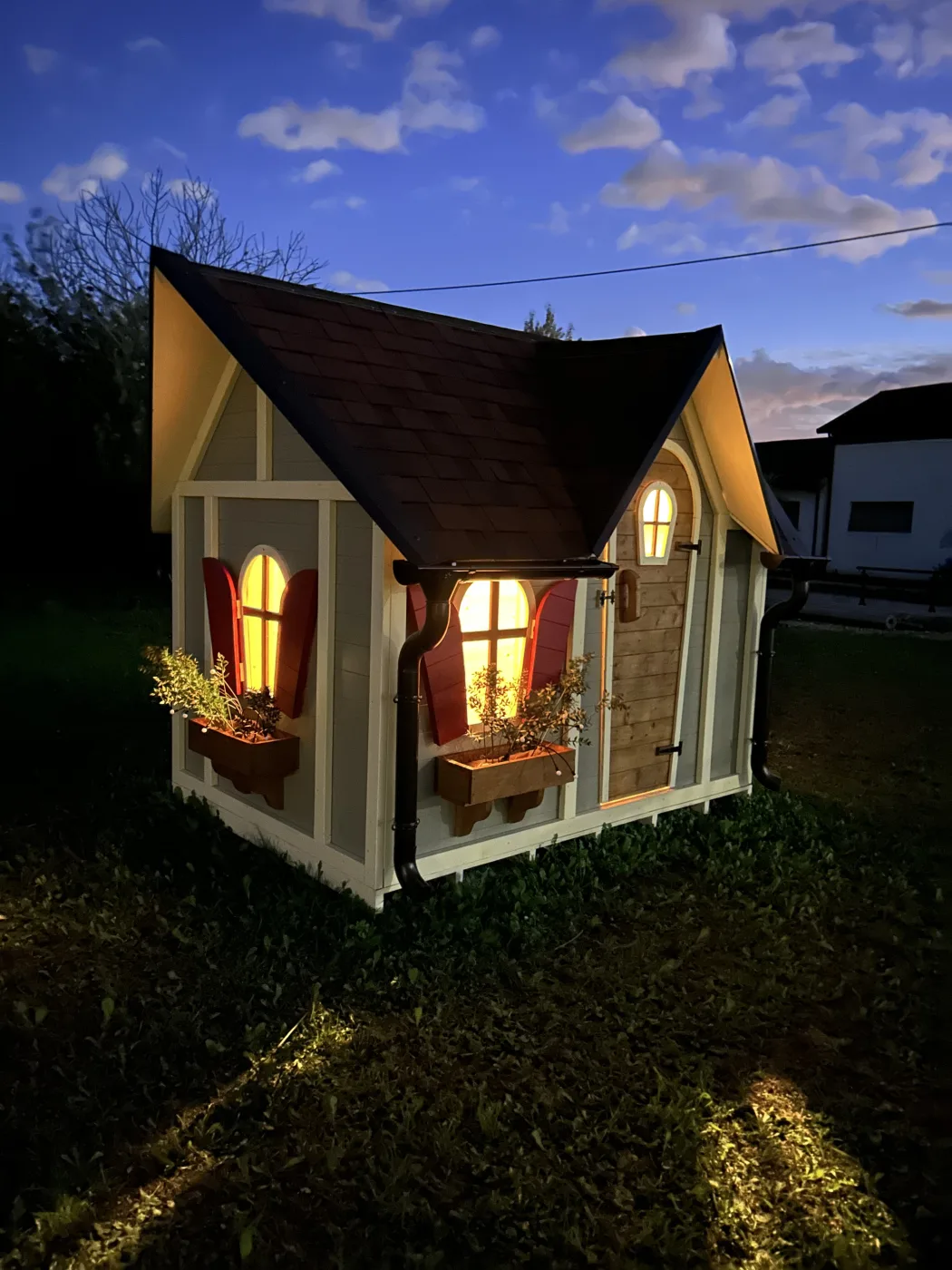 Casetta artigianale illuminata al tramonto con scuri rossi e fioriere.
