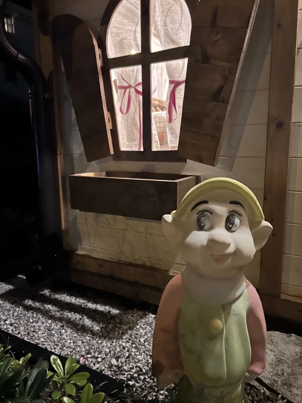 Statua del nano Cucciolo illuminata davanti alla finestra ad arco della casetta.