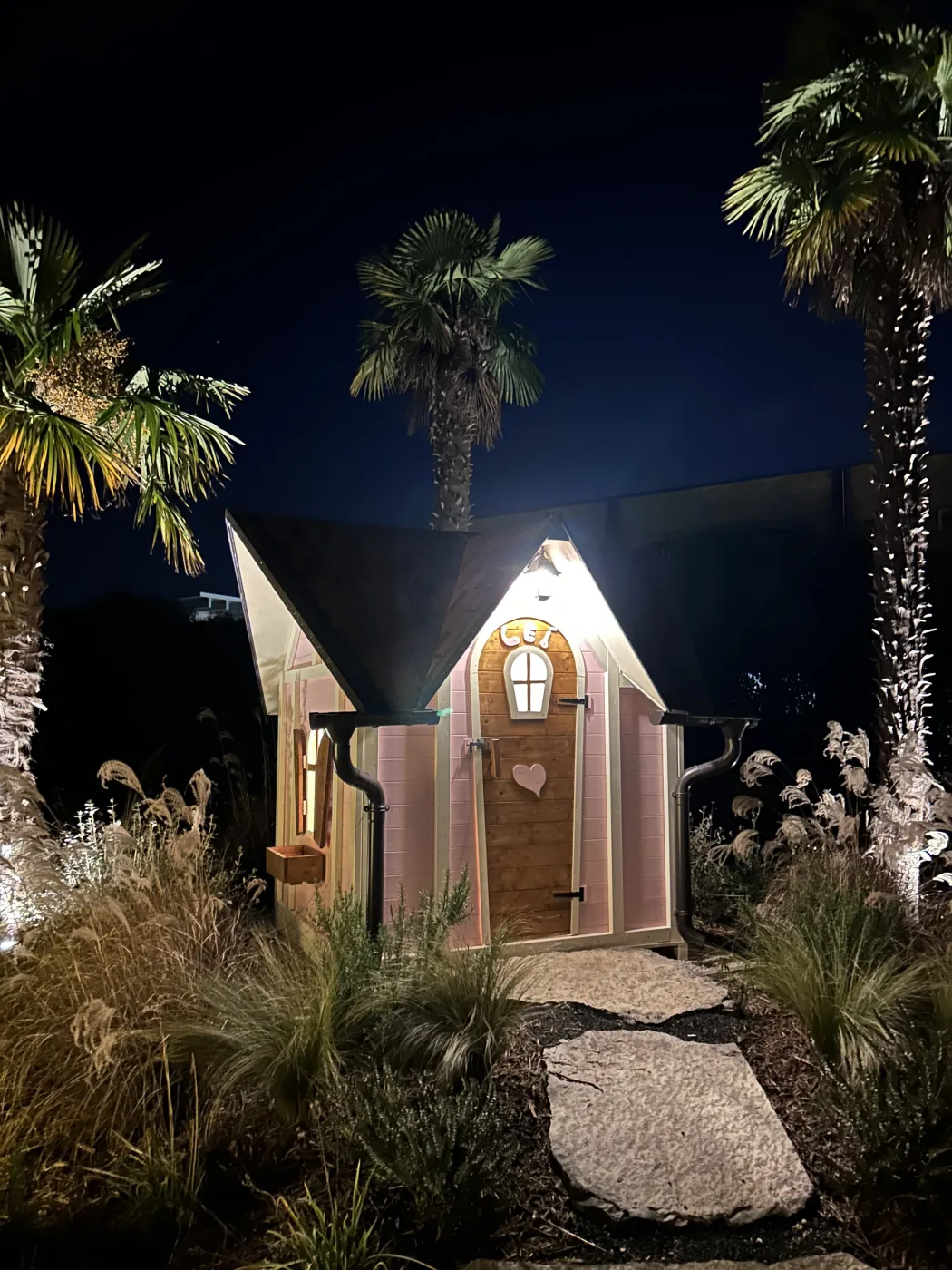 Casetta rosa illuminata di notte tra palme tropicali.