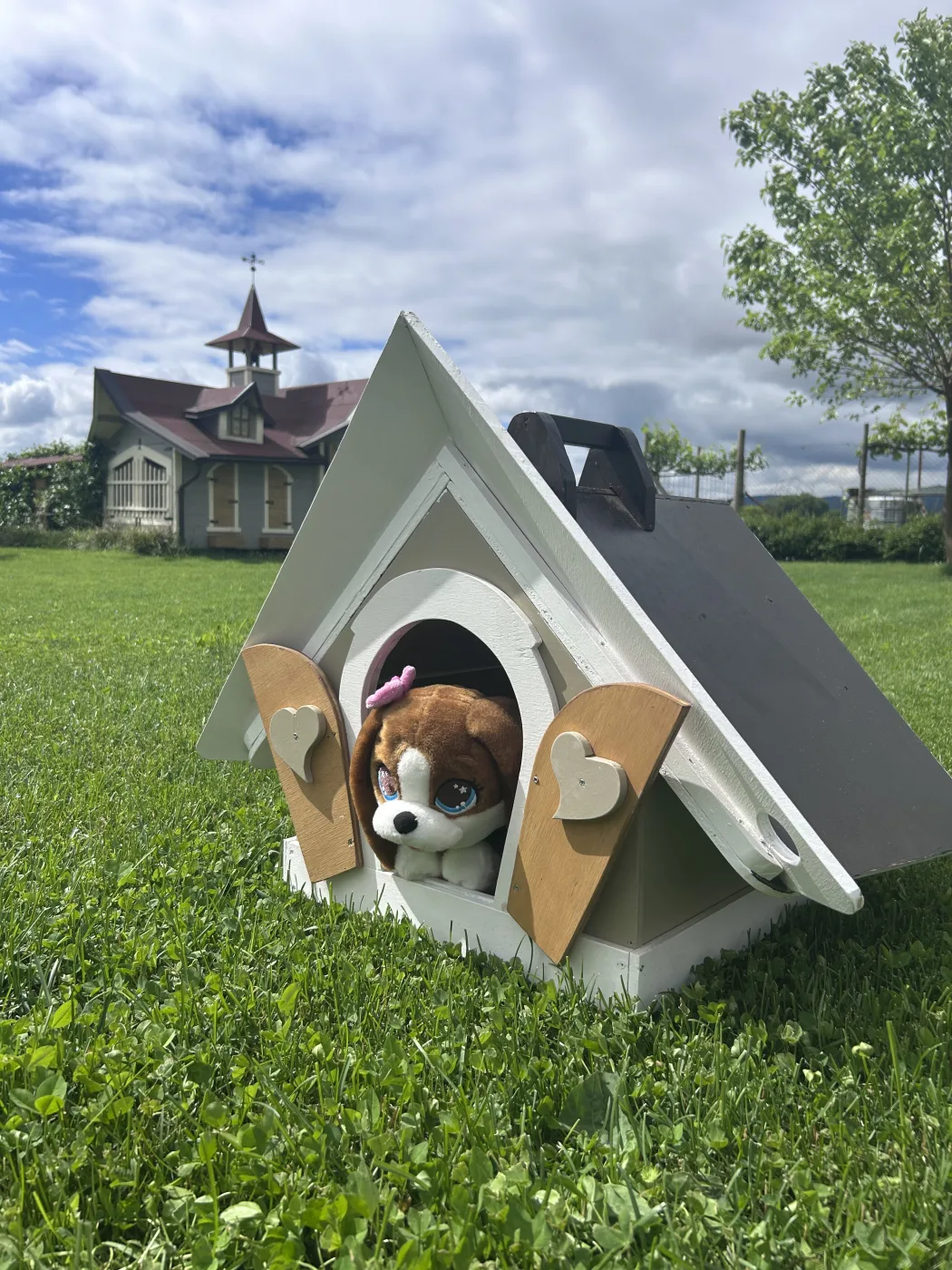 Cuccia in legno con peluche di cane, grande casetta fiabesca sullo sfondo nel prato.