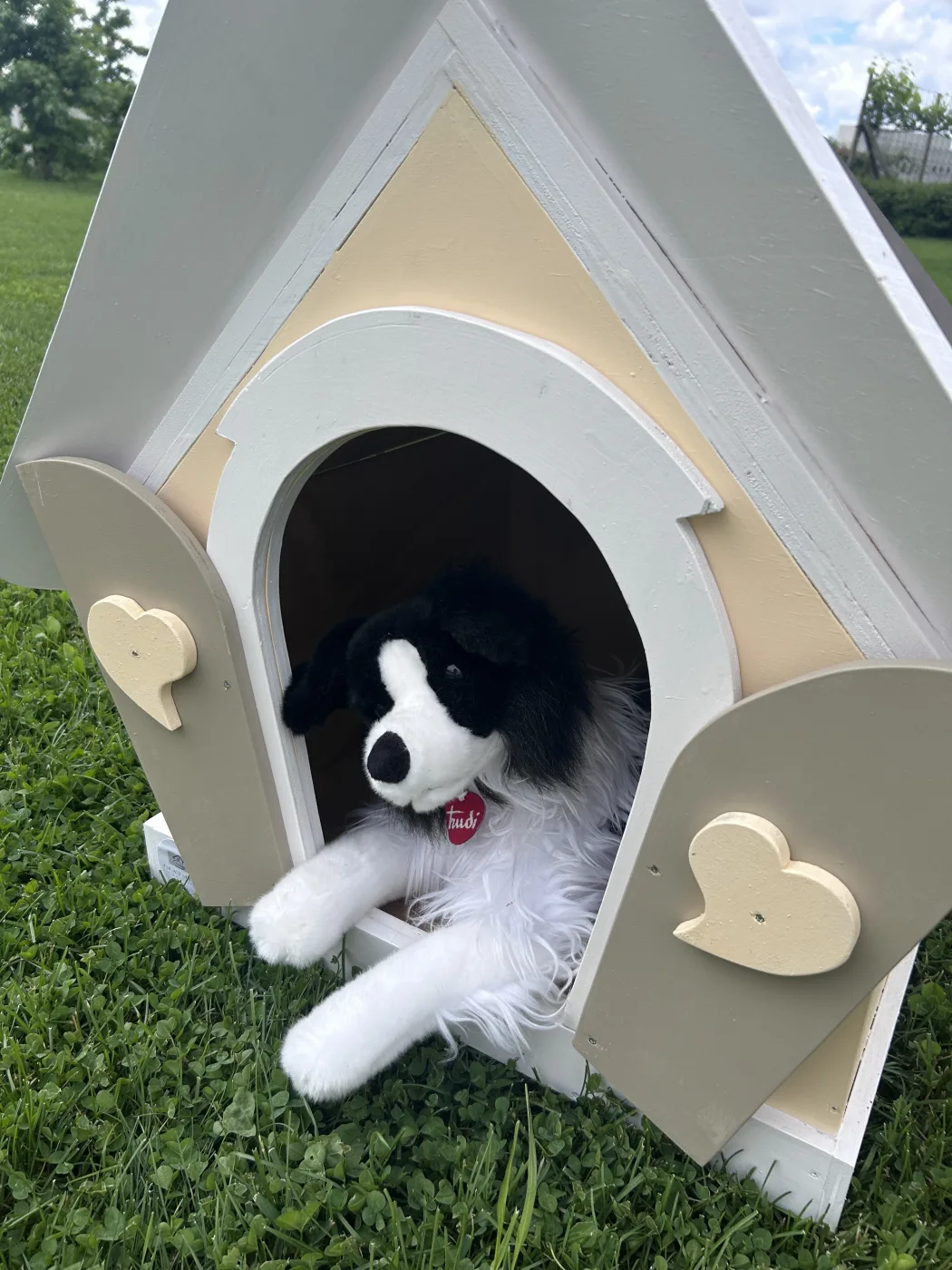 Peluche di cane border collie nella cuccia in legno con sportelli a cuore.