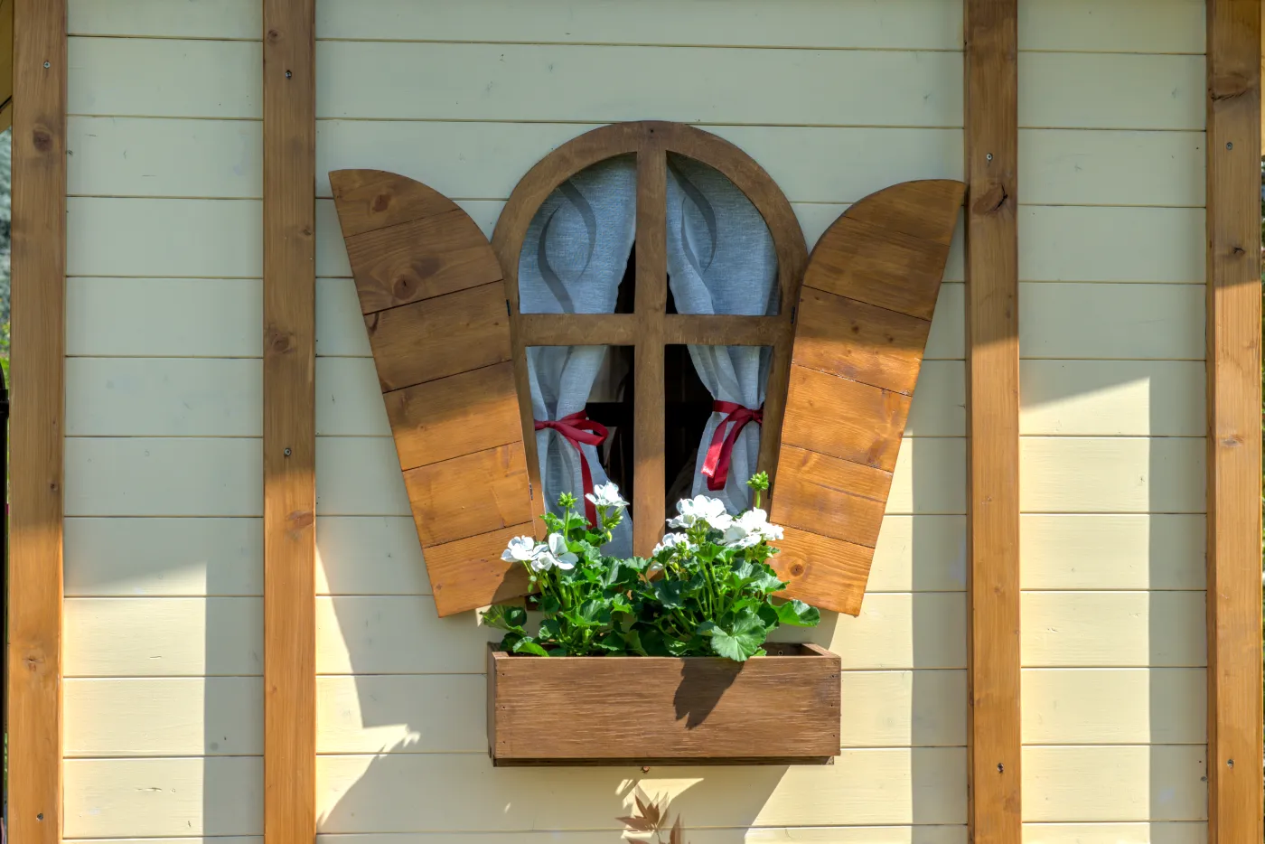 Finestra con scuri in legno e fiori bianchi nel davanzale.