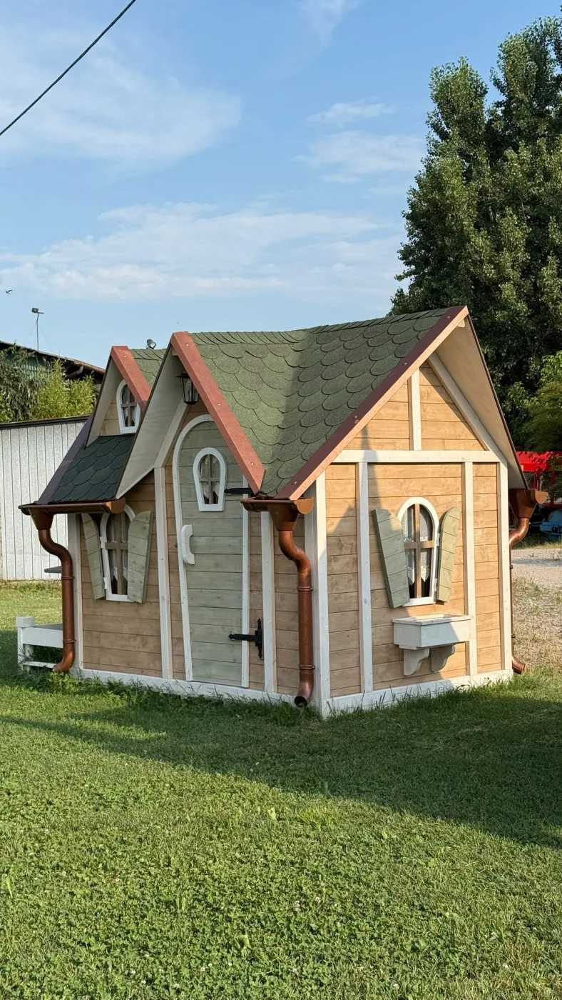 Casetta a tenda color tortora con tetto bordeaux, vista da lontano nel prato accanto a una balla di fieno e uno steccato bianco.
