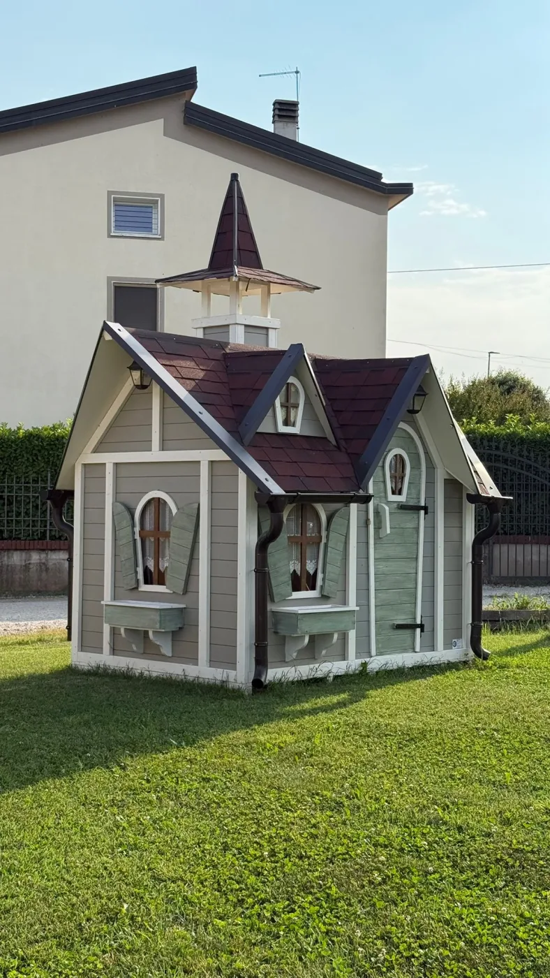 Casetta con mulino ad acqua decorativo in legno, ruota con scritta intagliata e recinzione bianca alla base.