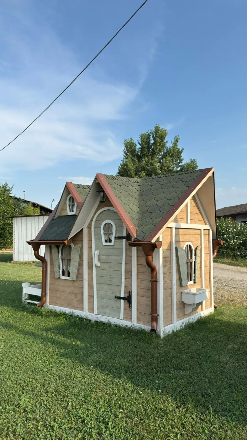Casetta con mulino ad acqua in legno, vista con edifici e uccelli in volo sullo sfondo.